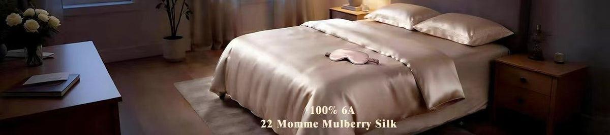 A bed dressed in shimmering champagne silk bedding with two pillows and a black eye mask, set in a softly lit bedroom. Text overlay reads: 'Luminous Dreams | 100% 6A 22 Momme Mulberry Silk | Midnight Glow Edition'.