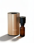 U-Scents waterless smart scent diffuser in Champagne Gold on a bamboo placemat, with an attached black nebulizing nozzle and a 10ml amber glass essential oil bottle.