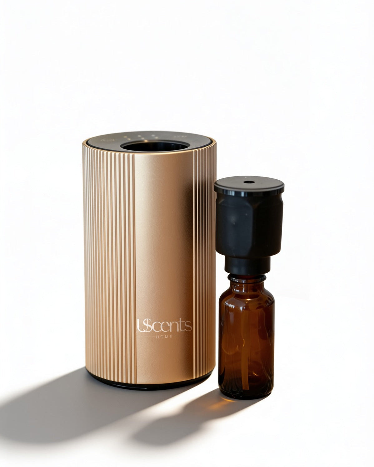 U-Scents waterless smart scent diffuser in Champagne Gold on a bamboo placemat, with an attached black nebulizing nozzle and a 10ml amber glass essential oil bottle.